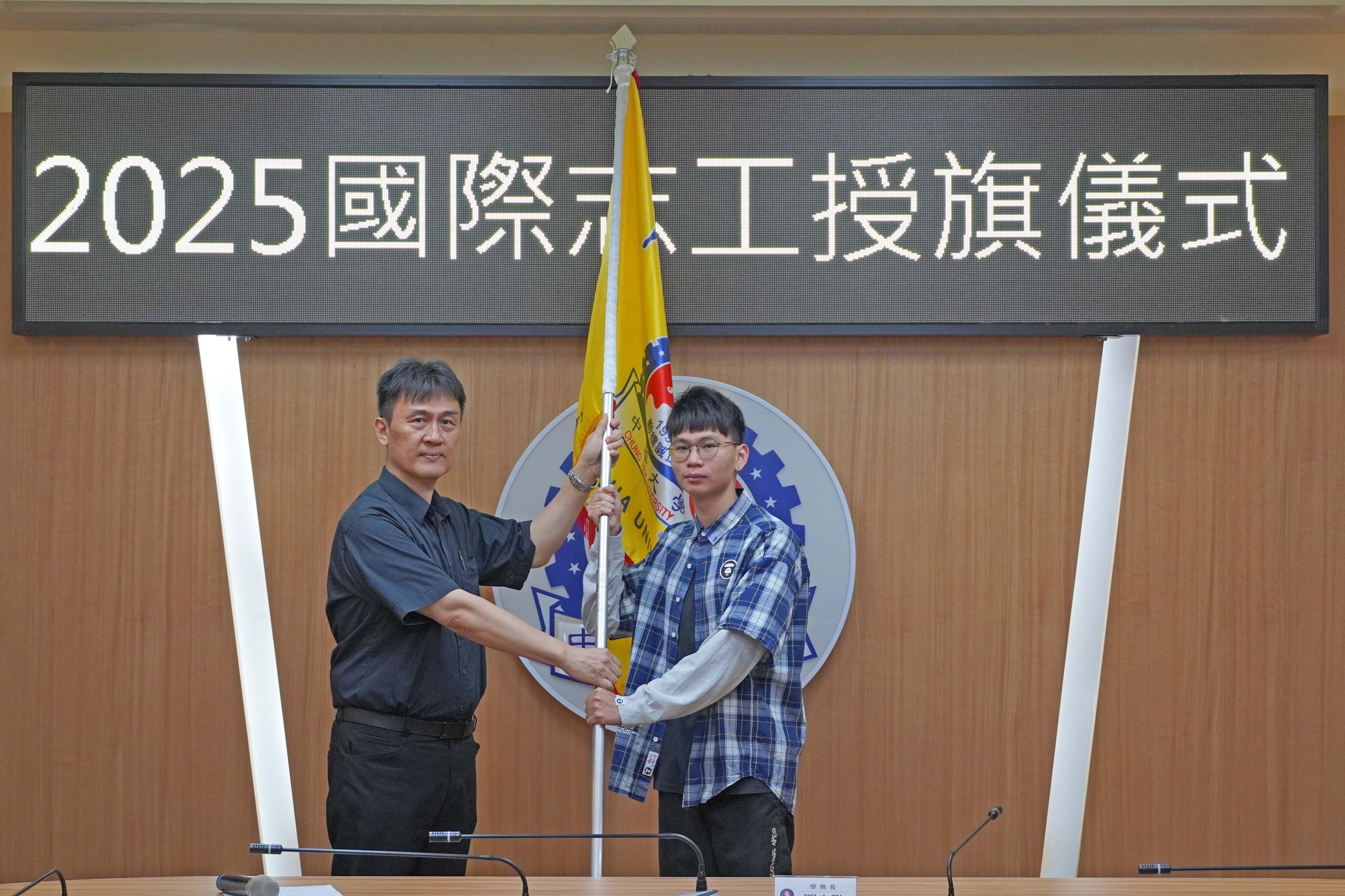 中華大學學務長閻克勤授旗給國際志工團團員林圭彥，祝福行程順利平安。